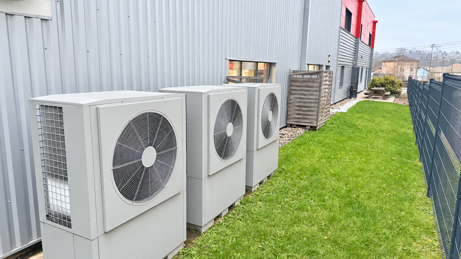 Trois unités extérieures à ventilateur alignées au pied d’un bâtiment à bardage métallique.